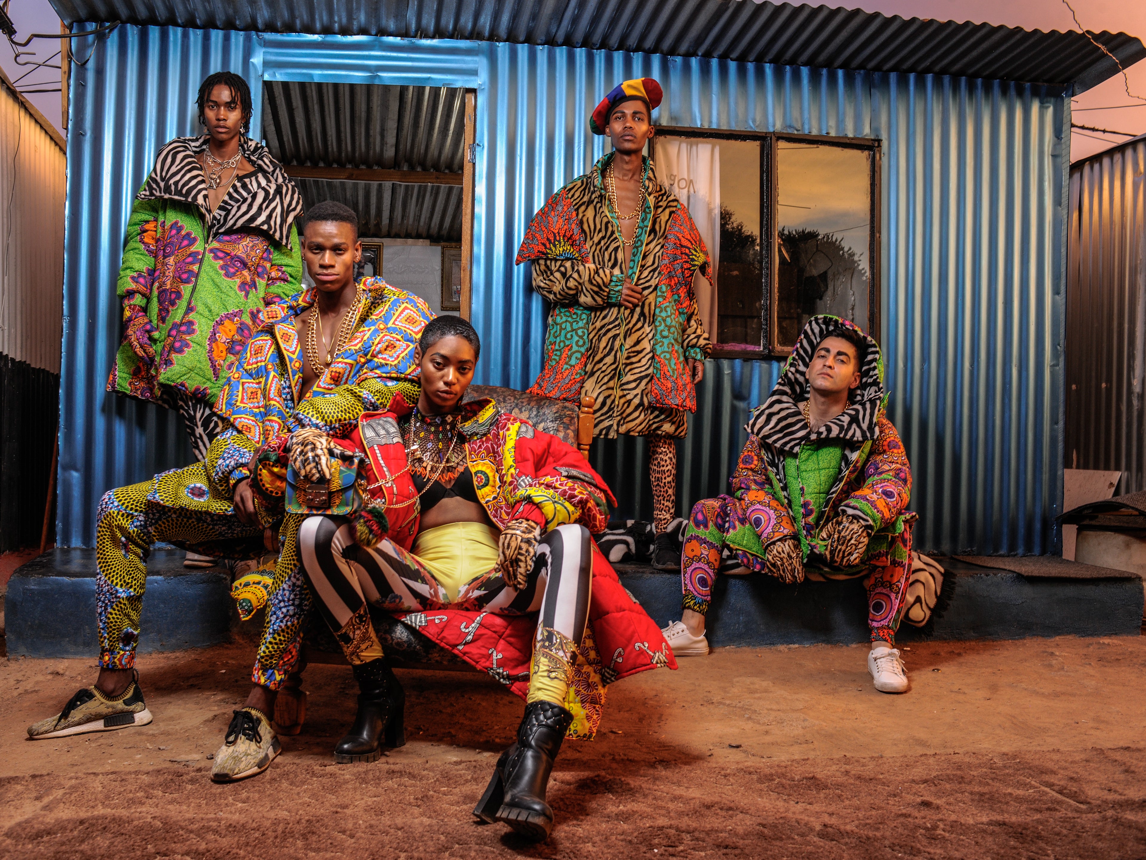 Five multi-racial models wearing vibrant, multicolored patterned BRAD AND ABIAH fashion outfits pose together in front of a corrugated blue metal house located in the Johannesburg township of Alexandra in South Africa.